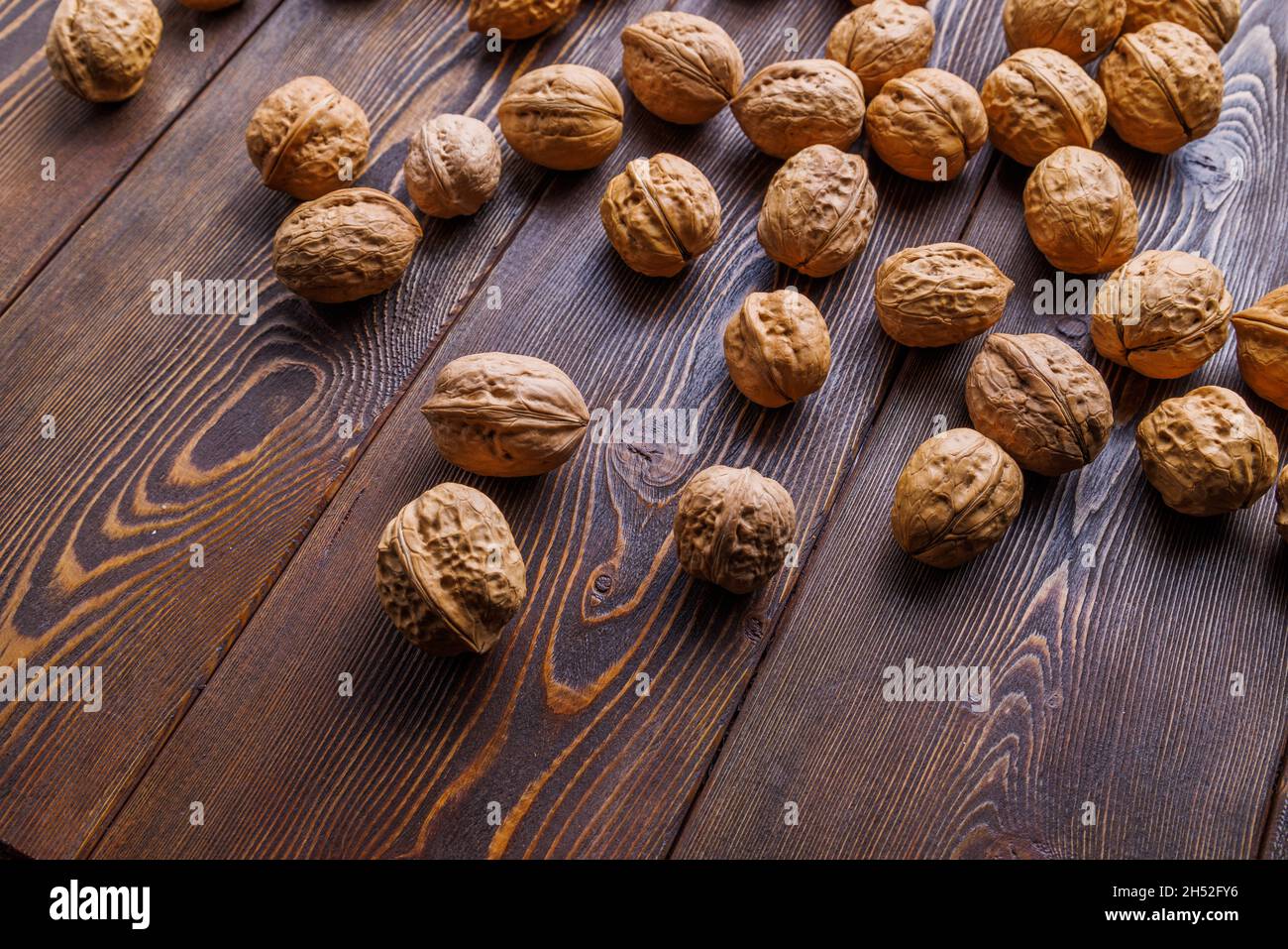 many walnuts with shells randomly scattered on brown wooden surface Stock Photo