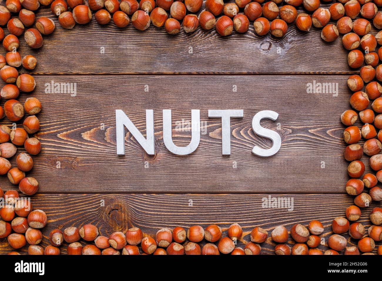 rectangular frame of many hazelnuts with shells on brown wooden surface