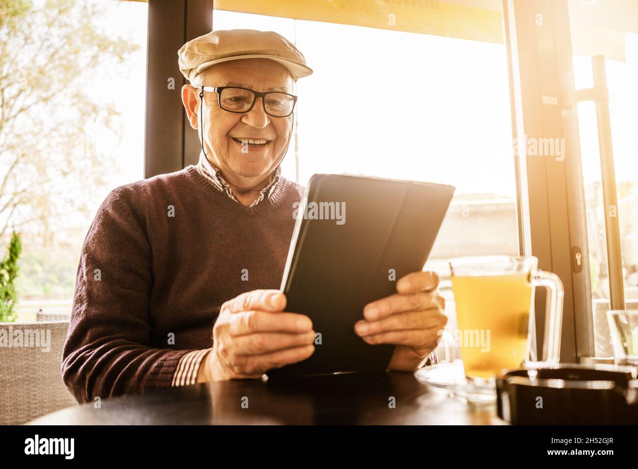 Senior man is sitting in cafe and using digital tablet. Stock Photo