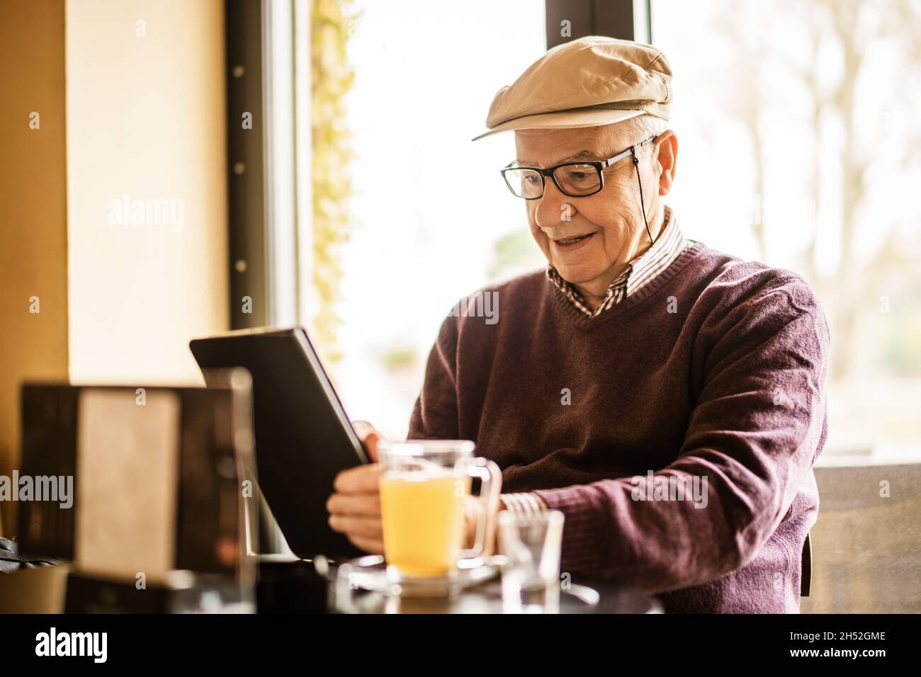 Senior man is sitting in cafe and using digital tablet. Stock Photo