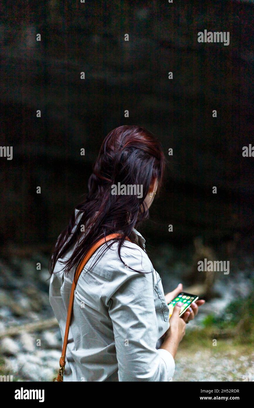 Long dark hair unrecognizable woman stay back using her smart phone. Rear view image. No face. Stock Photo