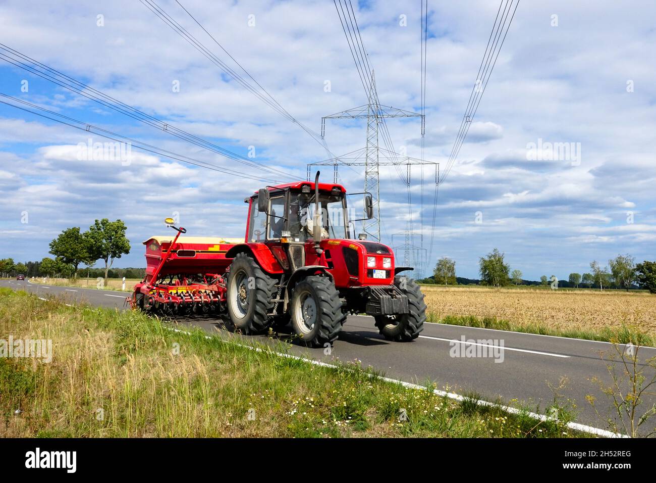 Seed drill tractor agricultural machine Germany farm and country road bellow powerlines Stock Photo
