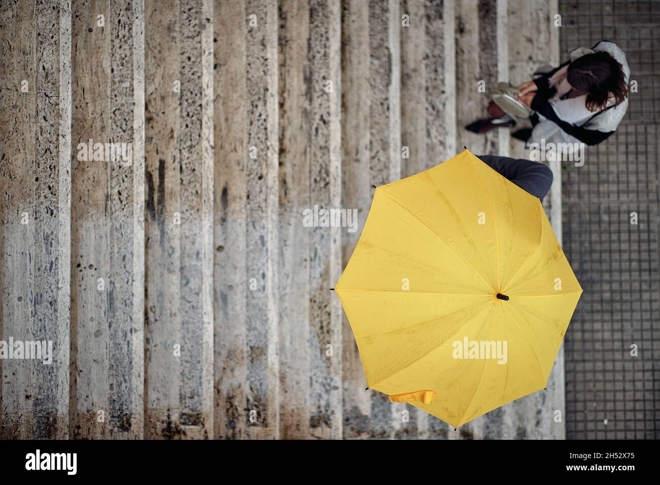 Bird-eye view of a young couple in love which is ascending the stairs in the city in a gloomy atmosphere during a rainy day. Walk, rain, city, relatio Stock Photo