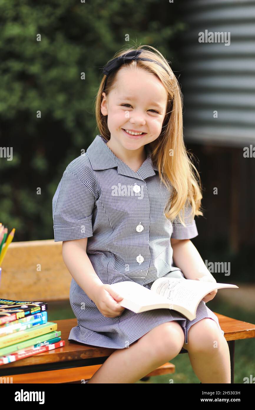 Back to school portrait image of little girl wearing uniform sitting at old style desk Stock Photo