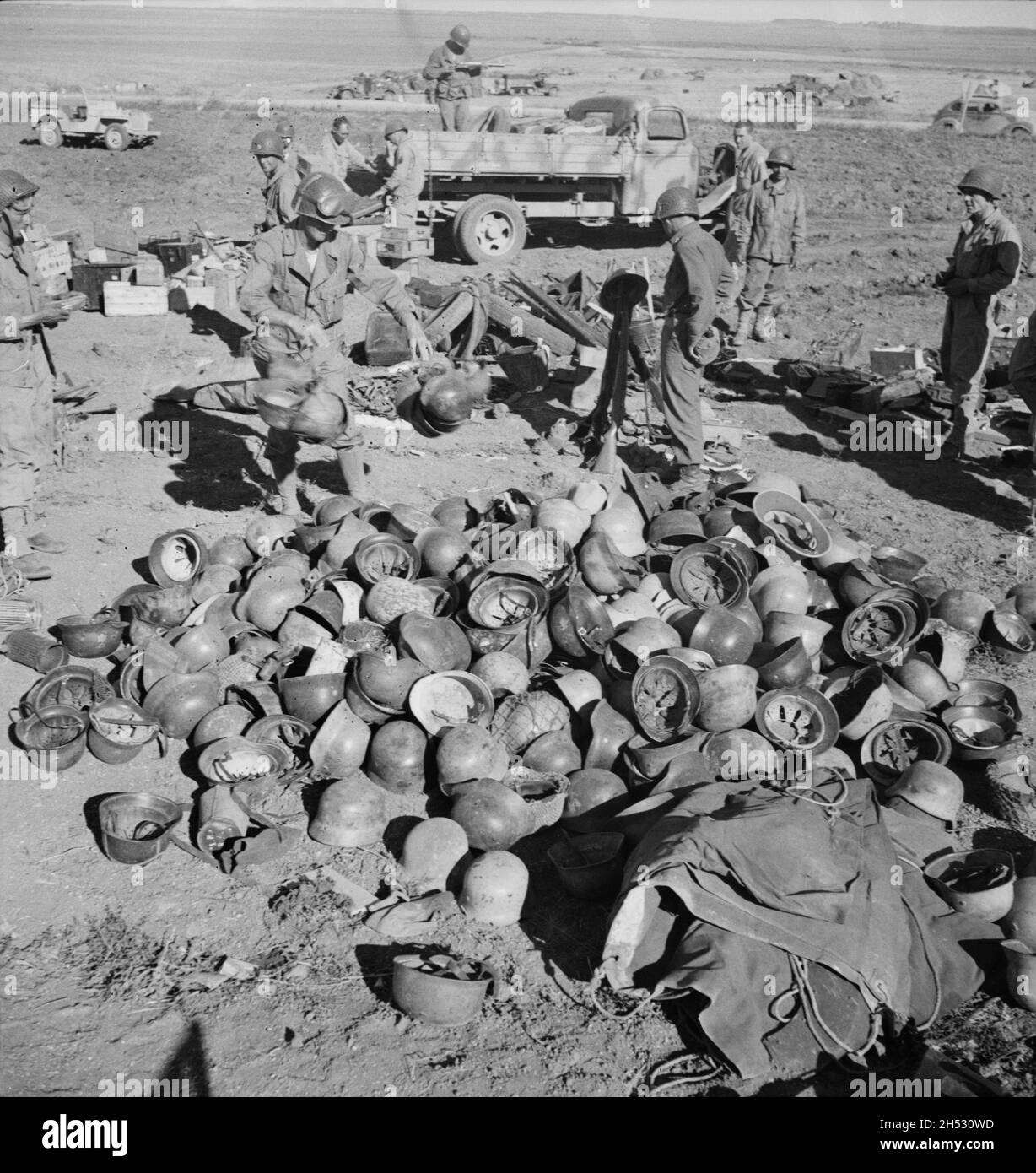 A vintage photo circa May 1943 of American soldiers piling up abandoned German helmets after the battle of Tunis and defeat of the German Afrika Korps Stock Photo