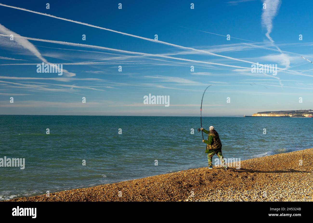 Casting on the beach under vapour trails Stock Photo