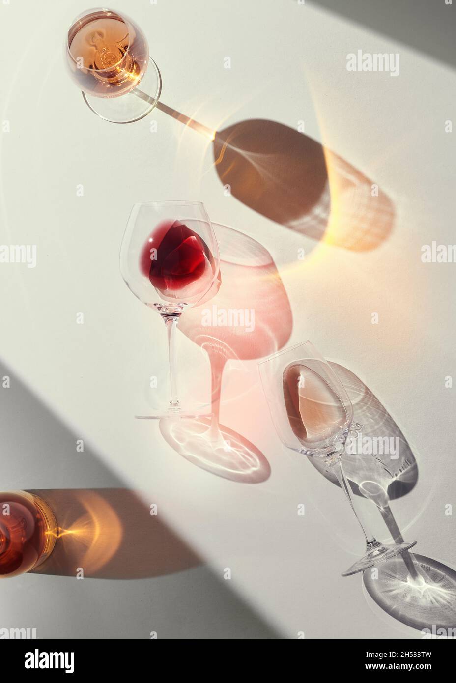 Glasses of red and rose wine on a white table. Strong emotional light with hard shadows. Moody and colorful  refractions. Stock Photo