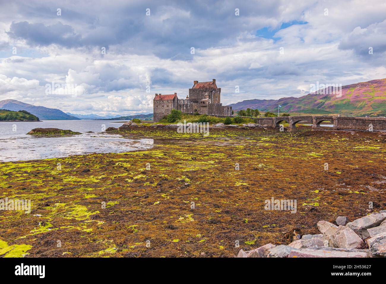 Old fortress in Scotland in the daytime with cloudy sky. Eilean Donan Castle in the Scottish Highlands at low tide. Historic stone bridge to the fortr Stock Photo