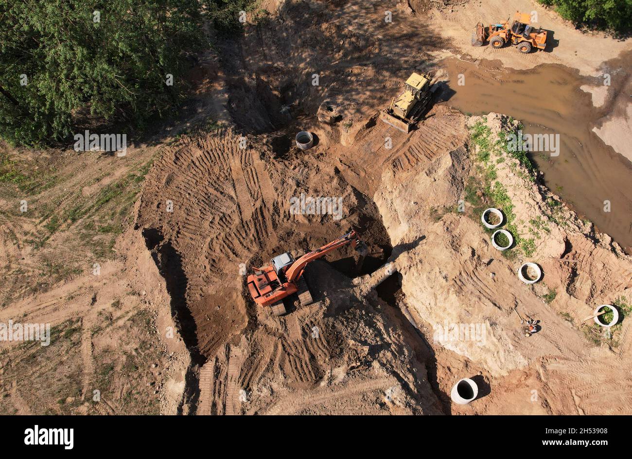 Laying of underground storm sewer pipes and sewerage well. Excavator at construction of water main, sanitary sewer, storm drain systems. Aerial view o Stock Photo