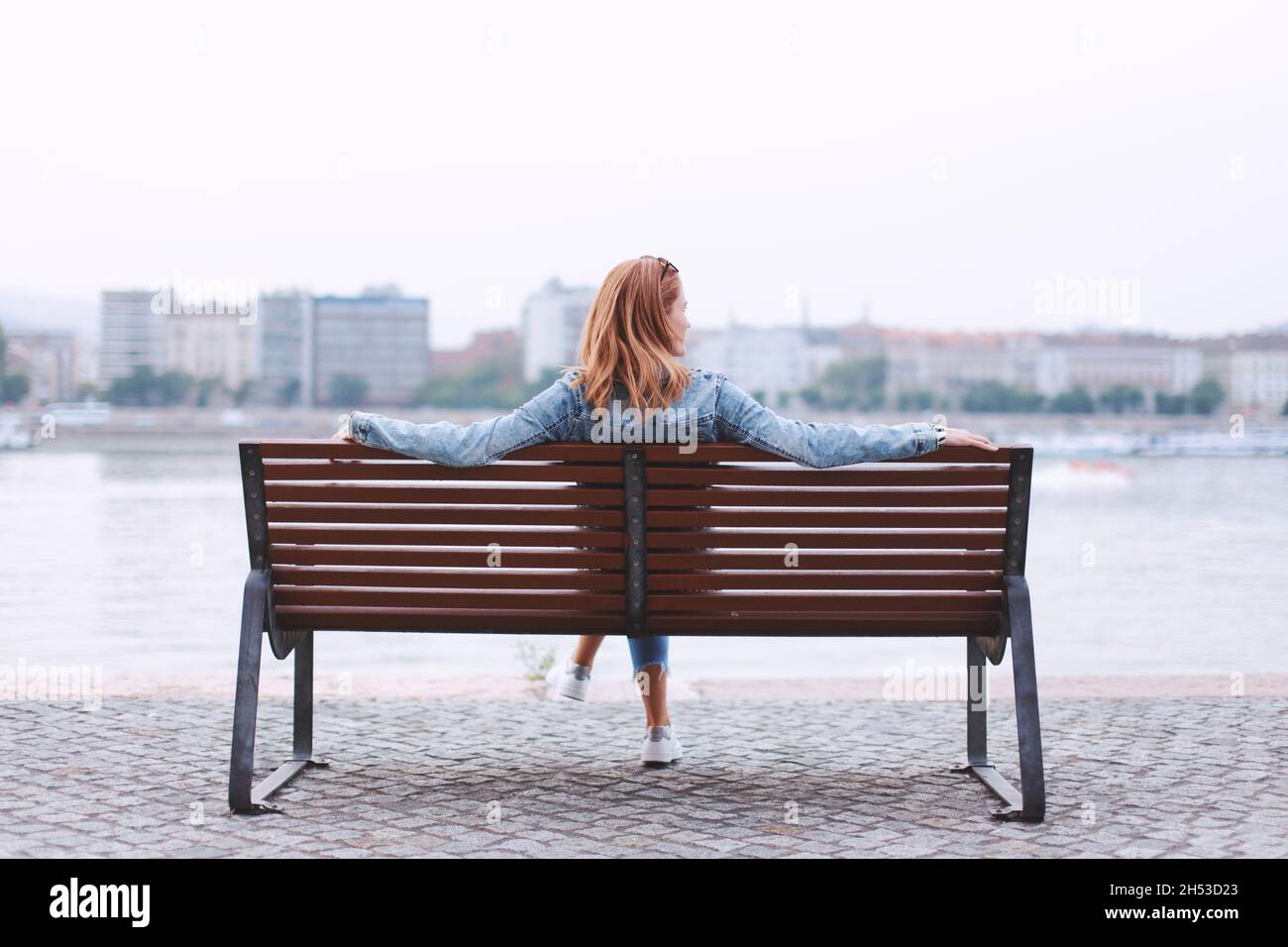 Young redhead woman relaxing on bench at riverside rear view Stock Photo
