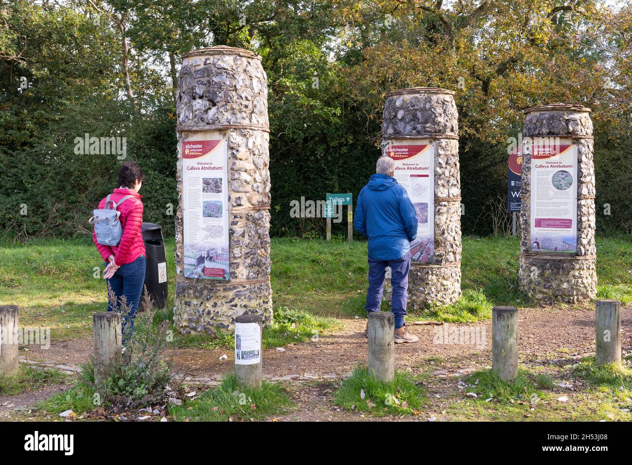A man and a woman reading visitor information on three vertical columns about the Silchester Roman City Walls (Calleva Atrebatum). Hampshire, UK Stock Photo