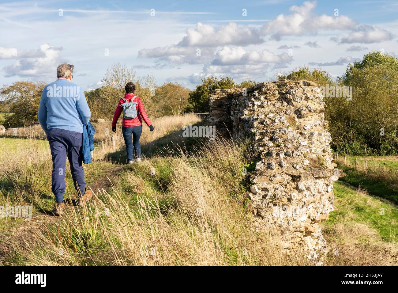 A couple of tourists - a married man and woman - walking next to a section of the ruined Roman town wall at Silchester. Hampshire, UK Stock Photo