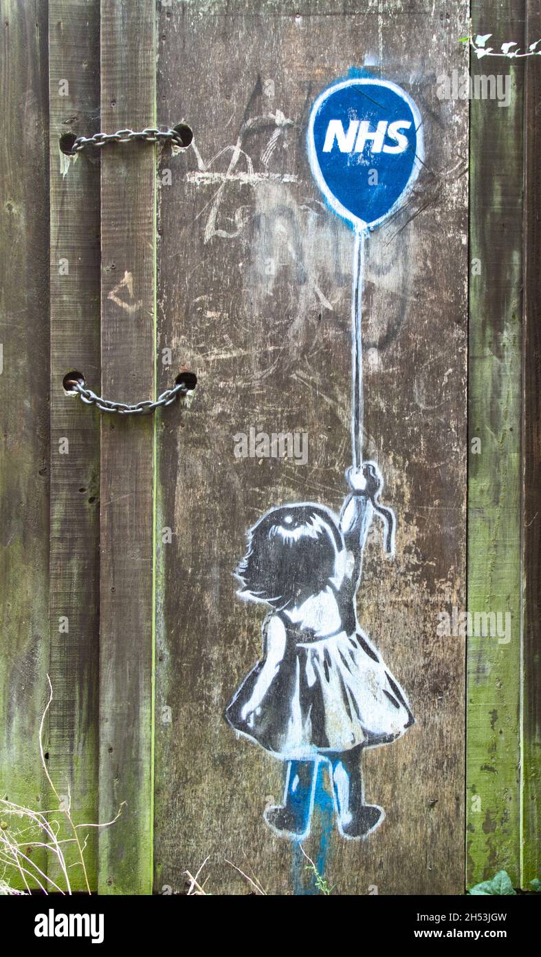 Painted Stencil On An Old Wooden Door Of the Back Of A Young Girl Holding A Balloon With NHS Printed On It, UK Stock Photo