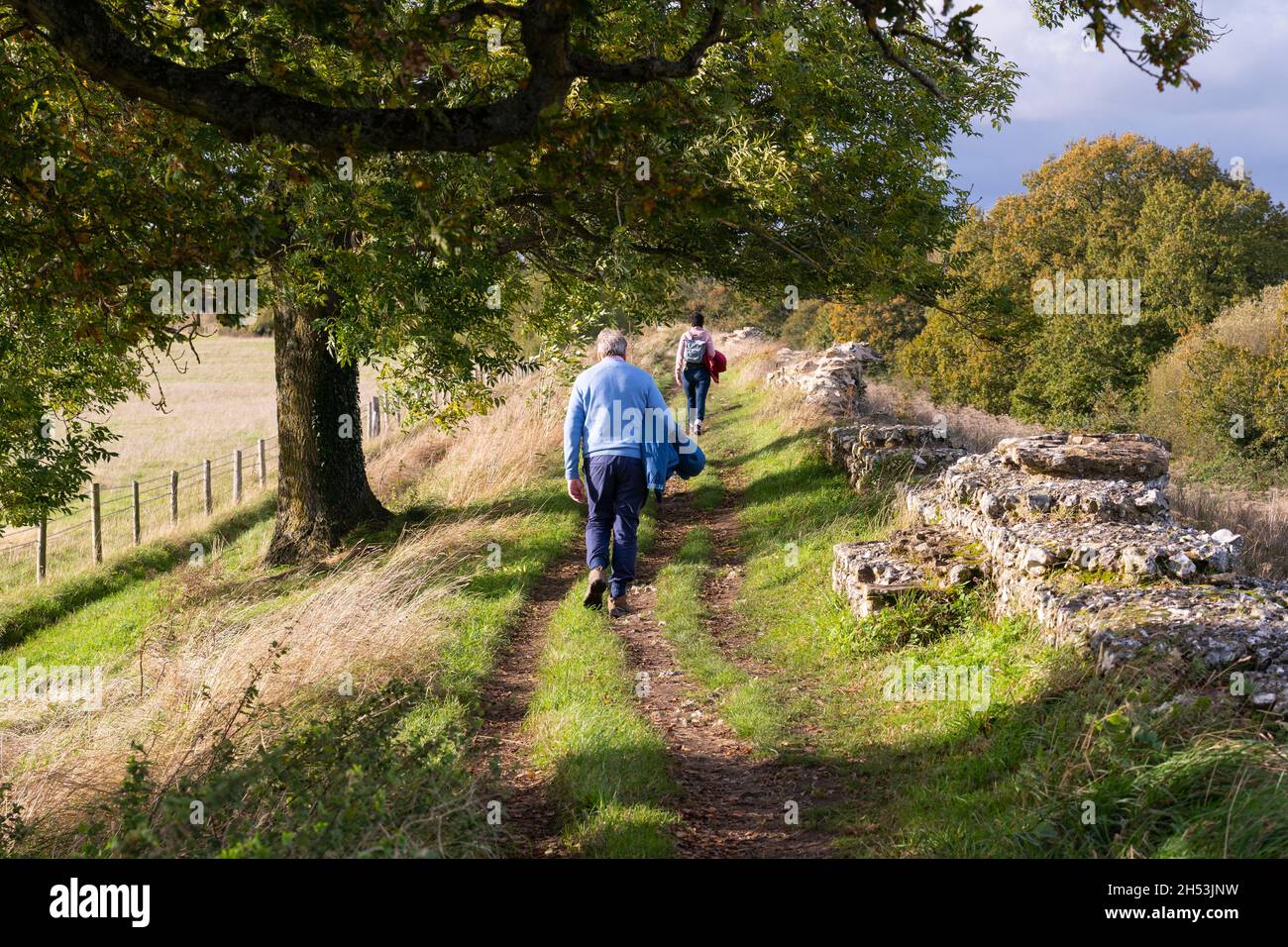 A couple of tourists - a married man and woman - walking next to a section of the ruined Roman town wall at Silchester in autumn. Hampshire, UK Stock Photo