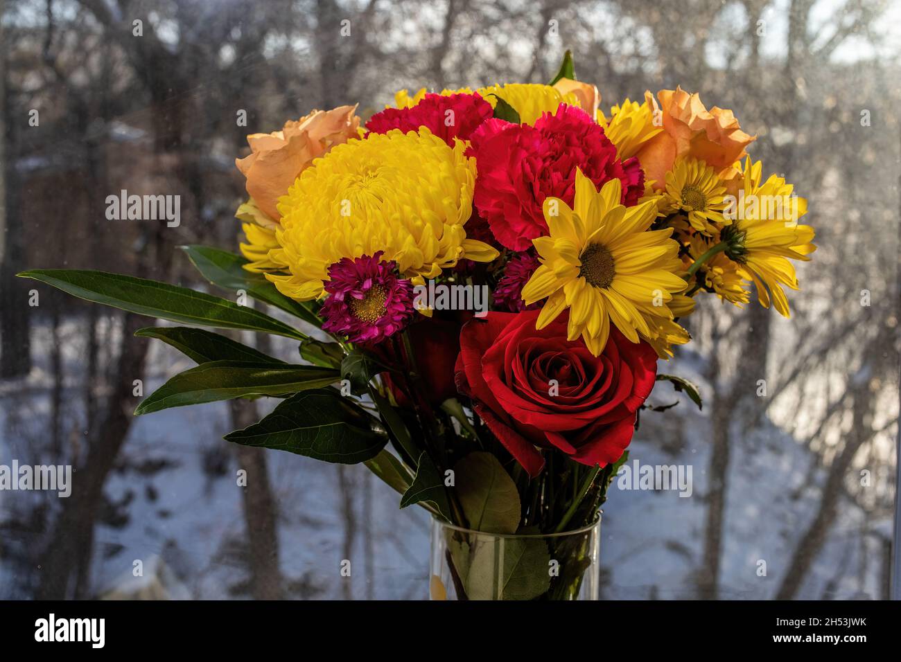 Beautiful flower arrangement in reds and yellow against a snowy background. Stock Photo