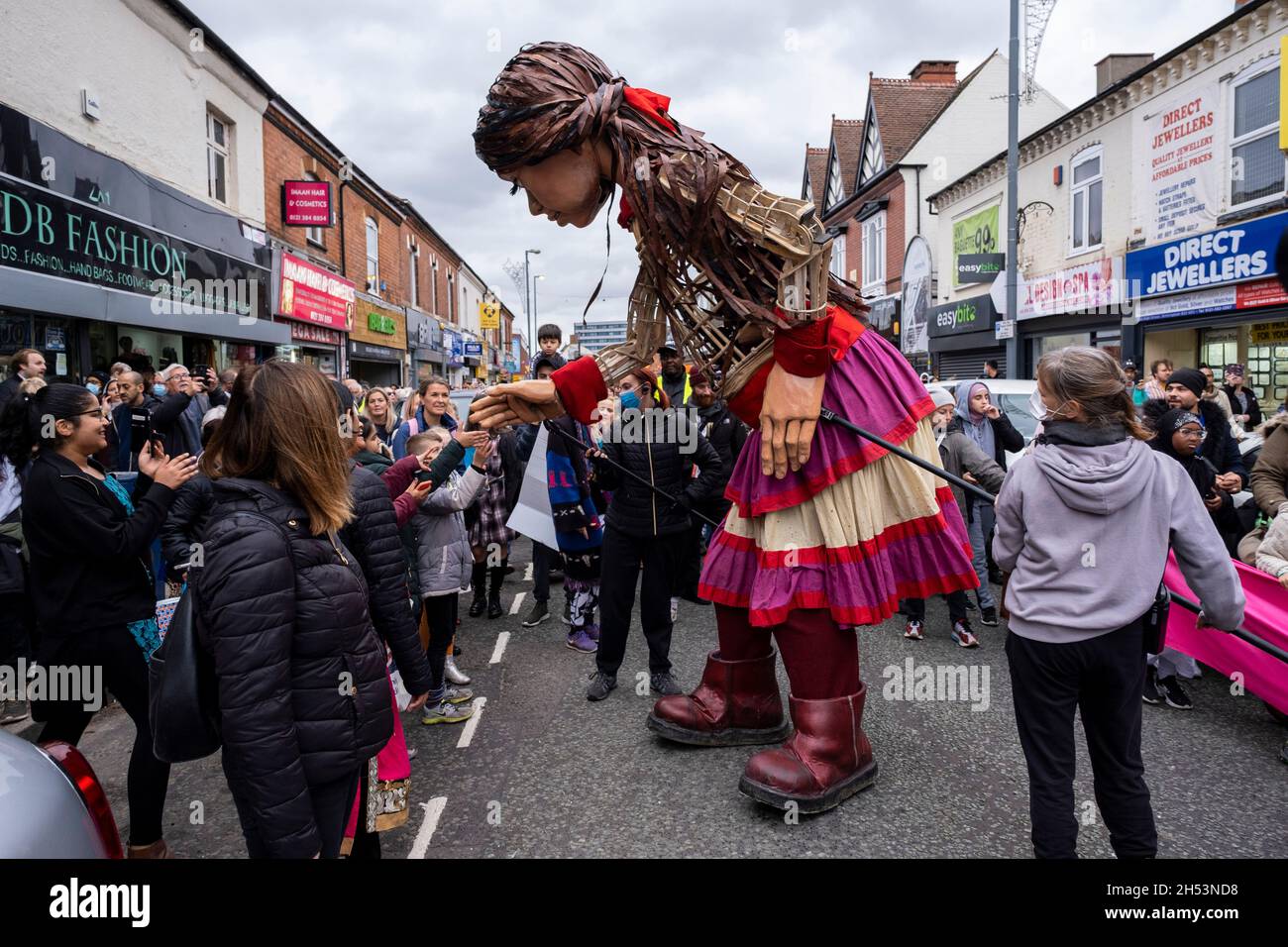 Little Amal delights crowds of onlookers as she walks along the High Street in Erdington on 28th October 2020 in Birmingham, United Kingdom. Little Amal is a 3.5 metre-tall puppet and living artwork of a young Syrian refugee child who has spent the last 3 months walking 8000 km from the boarder of Syria across Turkey, Greece, Italy, France, Switzerland, Germany, Belgium and the UK to focus attention on the urgent needs of young refugees. Stock Photo