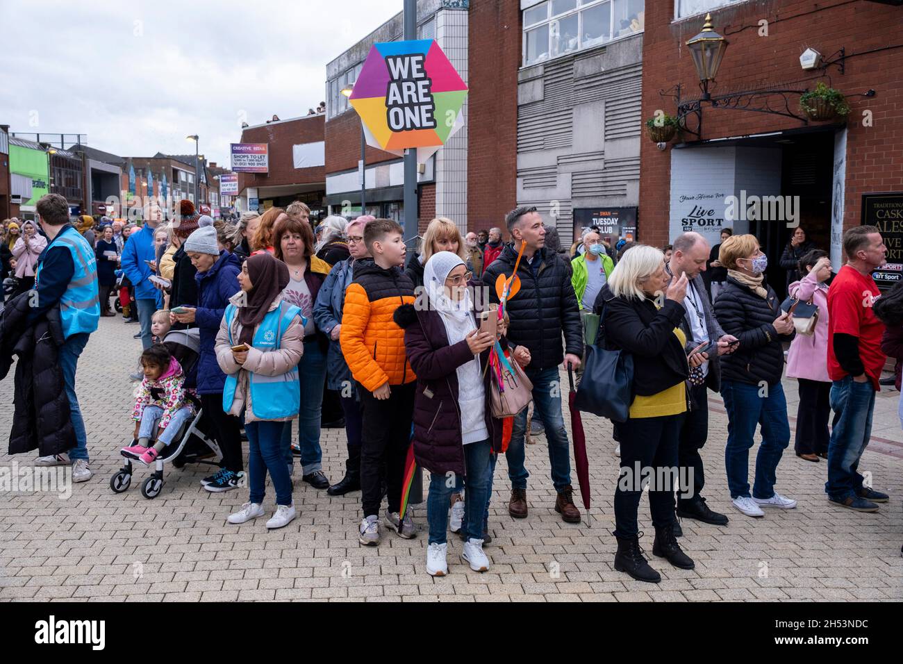 People wait for Little Amal before she walks along the High Street in Erdington on 28th October 2020 in Birmingham, United Kingdom. Little Amal is a 3.5 metre-tall puppet and living artwork of a young Syrian refugee child who has spent the last 3 months walking 8000 km from the boarder of Syria across Turkey, Greece, Italy, France, Switzerland, Germany, Belgium and the UK to focus attention on the urgent needs of young refugees. Stock Photo