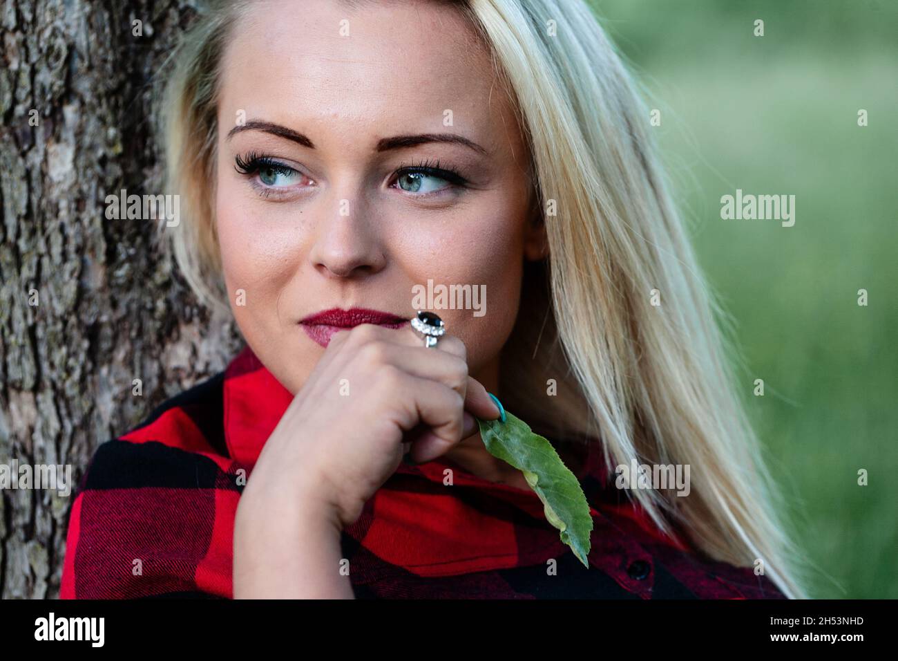 Young Blond Woman Looks To The Left While Leaning Against A Tree She