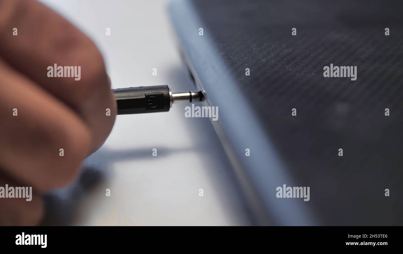 Headphone wire inserted into laptop. Media. Closeup of man inserting