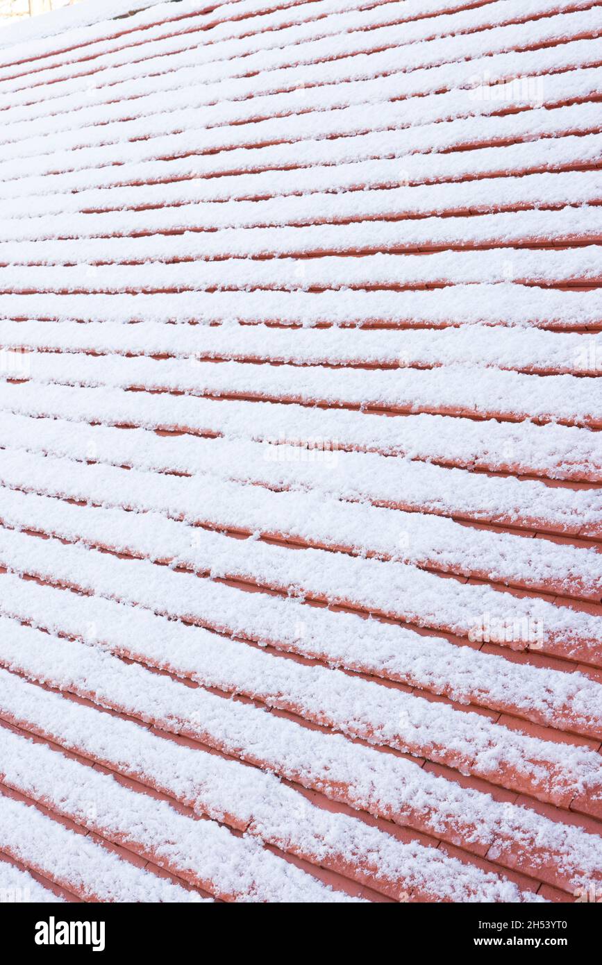 Detail of pitched roof with new plain clay roof tiles covered in snow in winter, UK Stock Photo