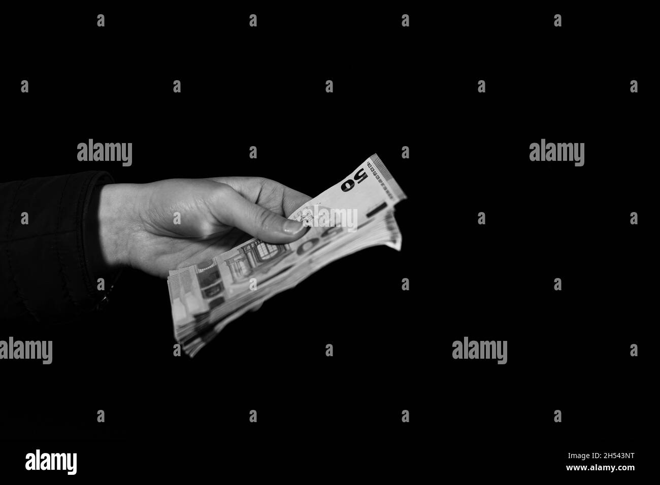 Grayscale of a human hand giving money - holding EURO on a black background Stock Photo