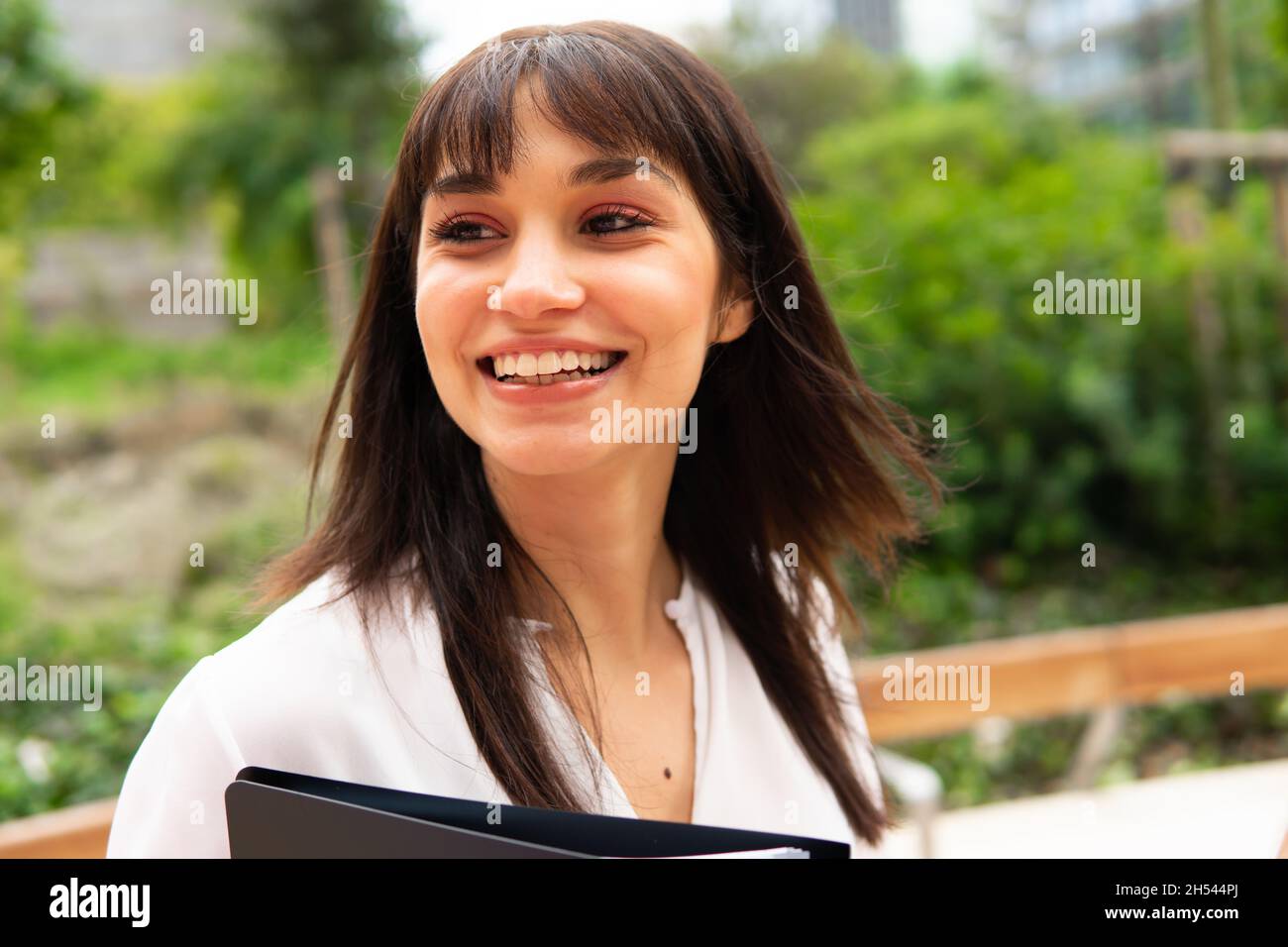 Cheerful female manager smiling and looking away while standing on blurred background of park Stock Photo