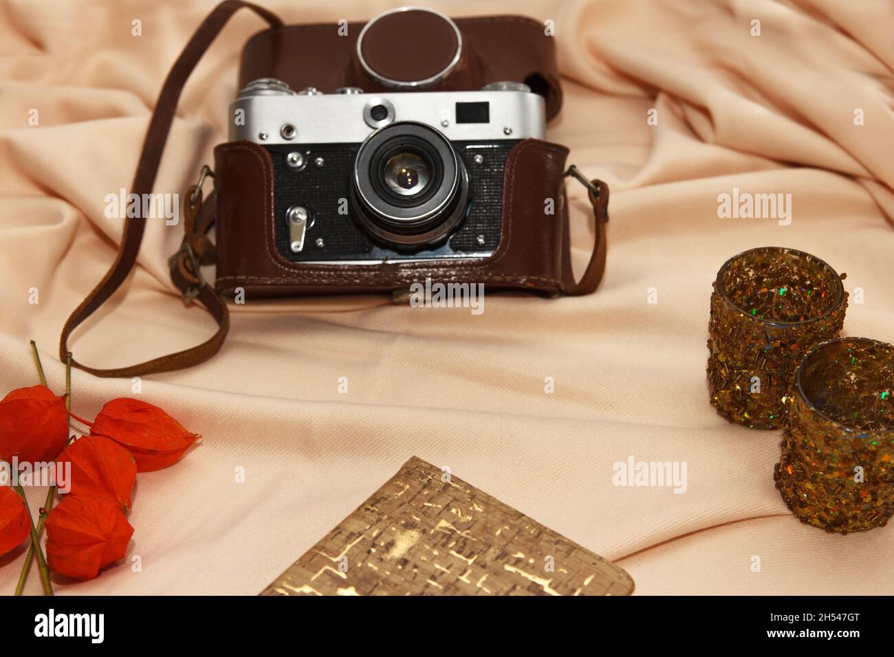 Flatlay. Film camera in case, notebook, fisalis and candlesticks lie on a light beige background. Stock Photo