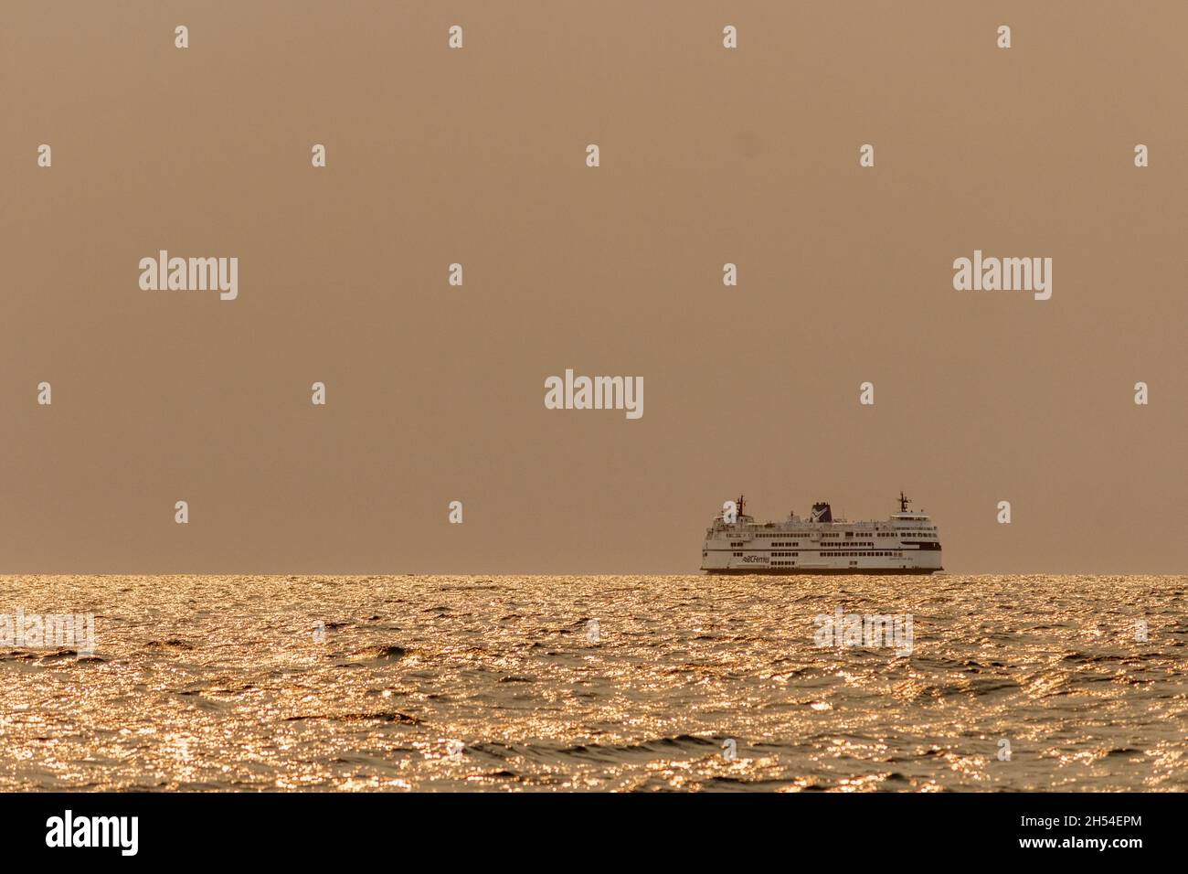 A passenger ferry crosses the Strait of Georgia on a summer morning, with thick smoke from wildfires obscuring the sun and turning sea and sky orange. Stock Photo