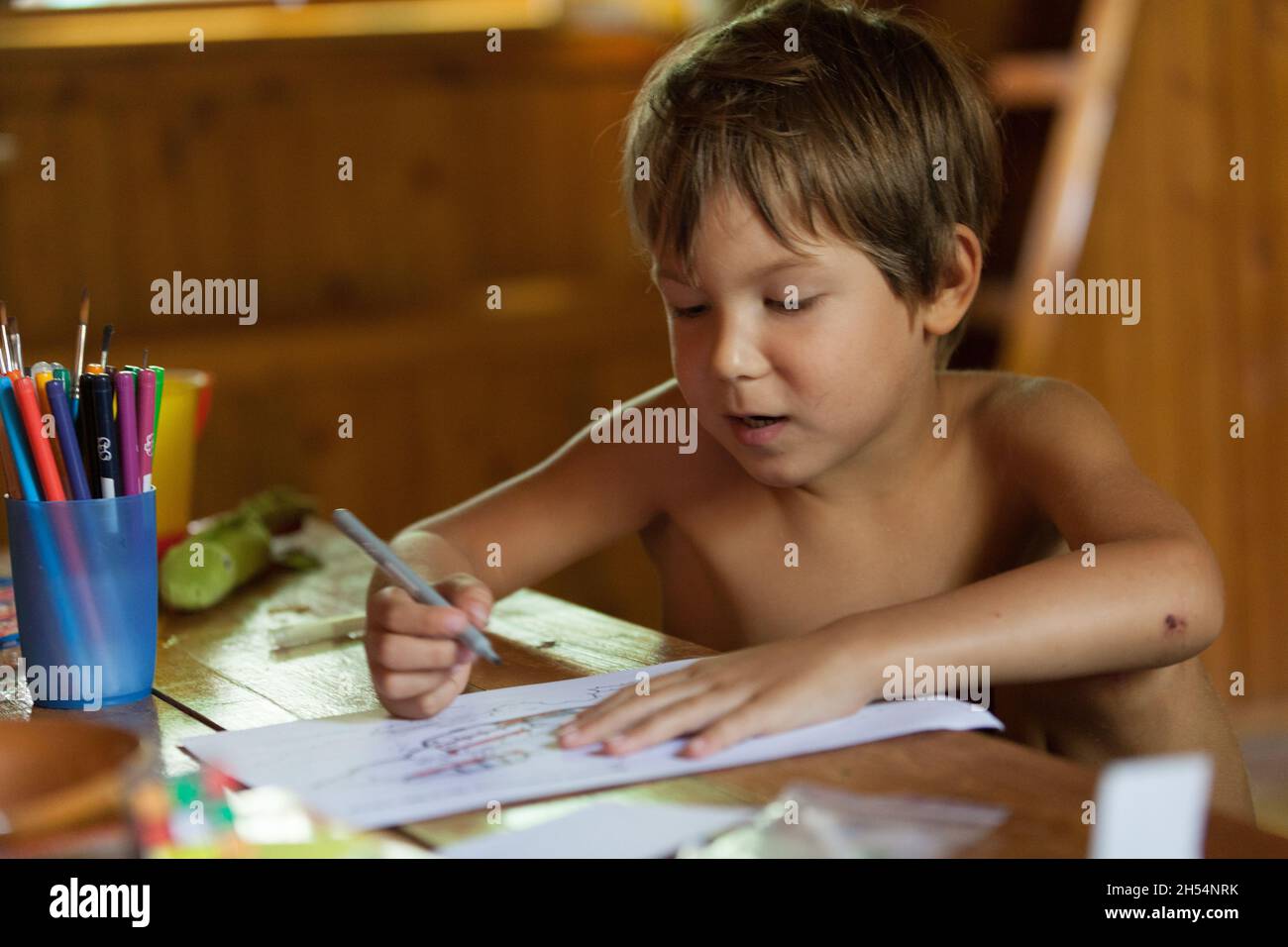 A boy is looking and singing while painting on a white paper Stock Photo