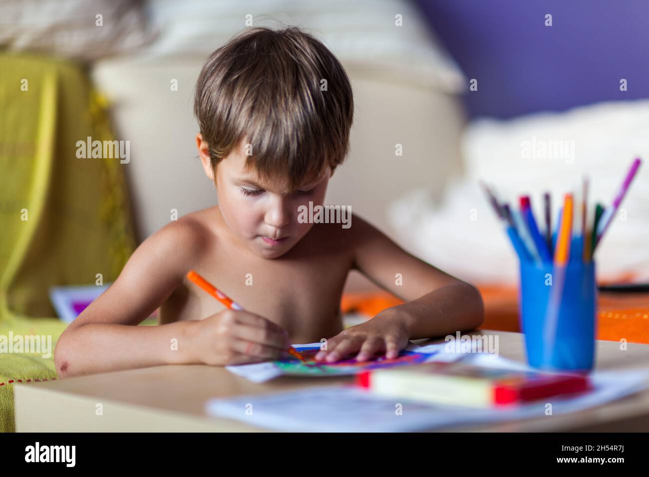 A boy is looking and singing while painting on a white paper Stock Photo
