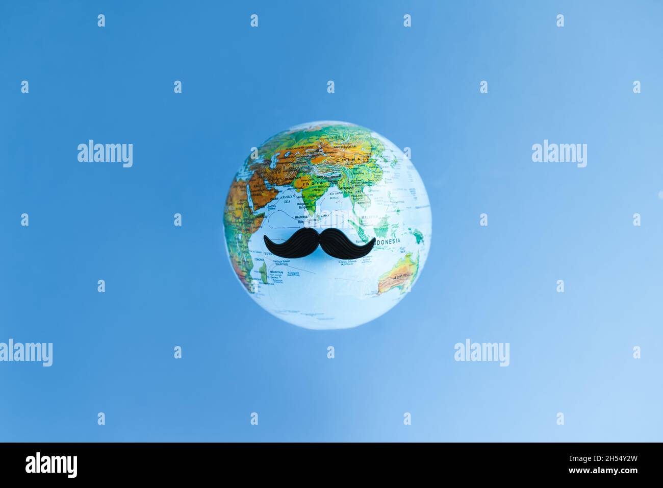 Top view creative flatlay background of Movember concept. Black moustaches on planet Earth on blue background. Men health awareness month, fathers day Stock Photo