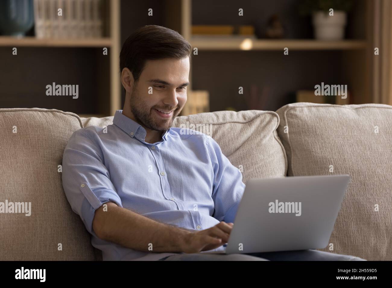 Smiling millennial handsome guy using laptop at home. Stock Photo