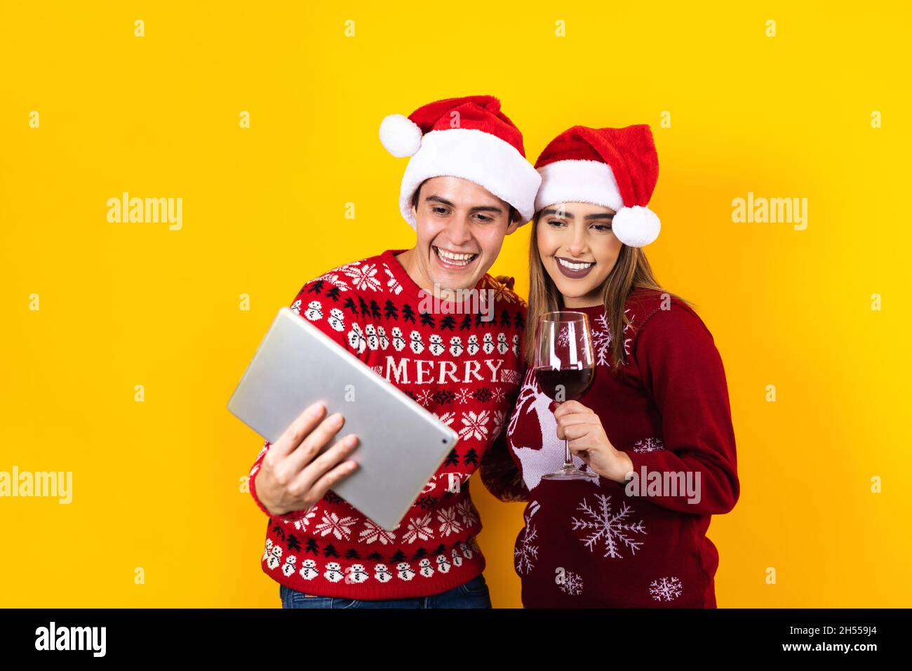 young latin couple having christmas video call using digital tablet or touchpad on a yellow background Stock Photo