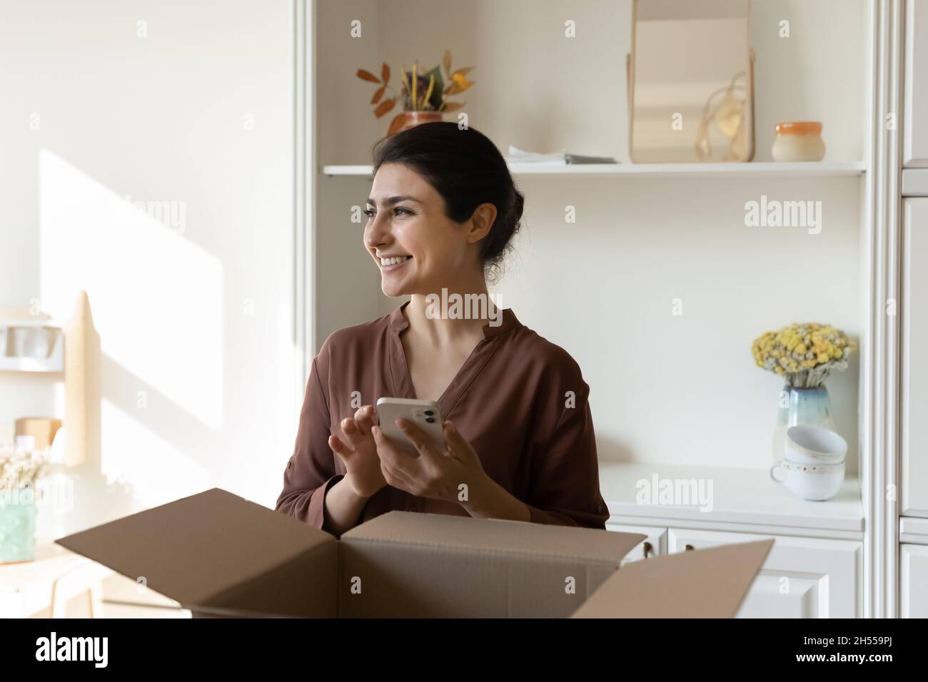Indian client of ecommerce holds phone looks aside feels satisfied Stock Photo