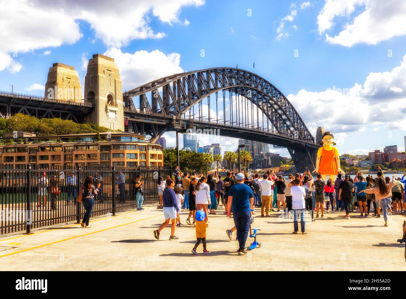 Sydney, Australia – 31 Oct 2021: Squid game doll near Harbour Bridge with crowd playing red light green light and taking photos. Stock Photo