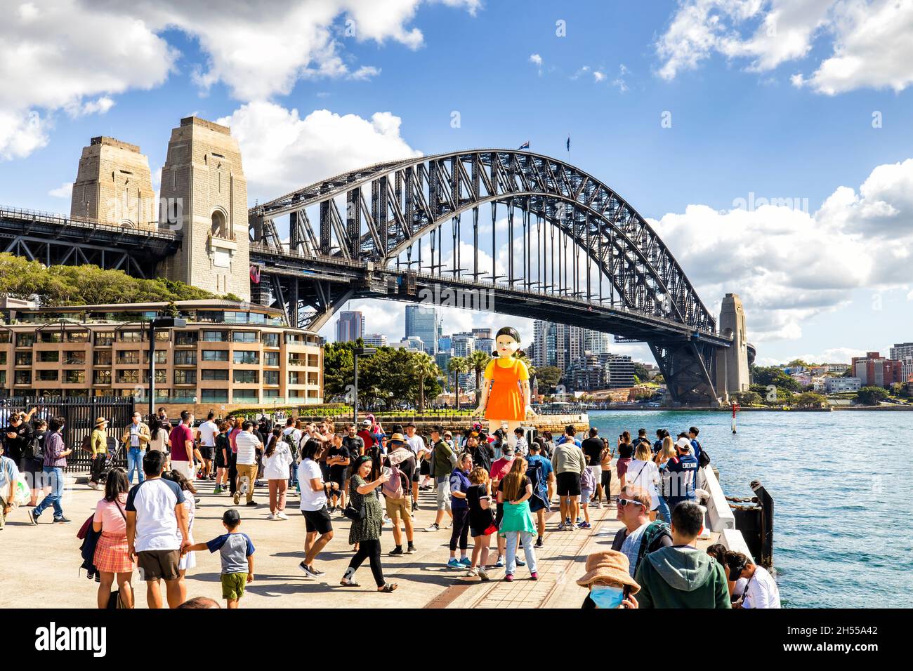 Sydney, Australia – 31 Oct 2021: Squid game doll near Harbour Bridge in the Rocks with crowd of spectators. Stock Photo