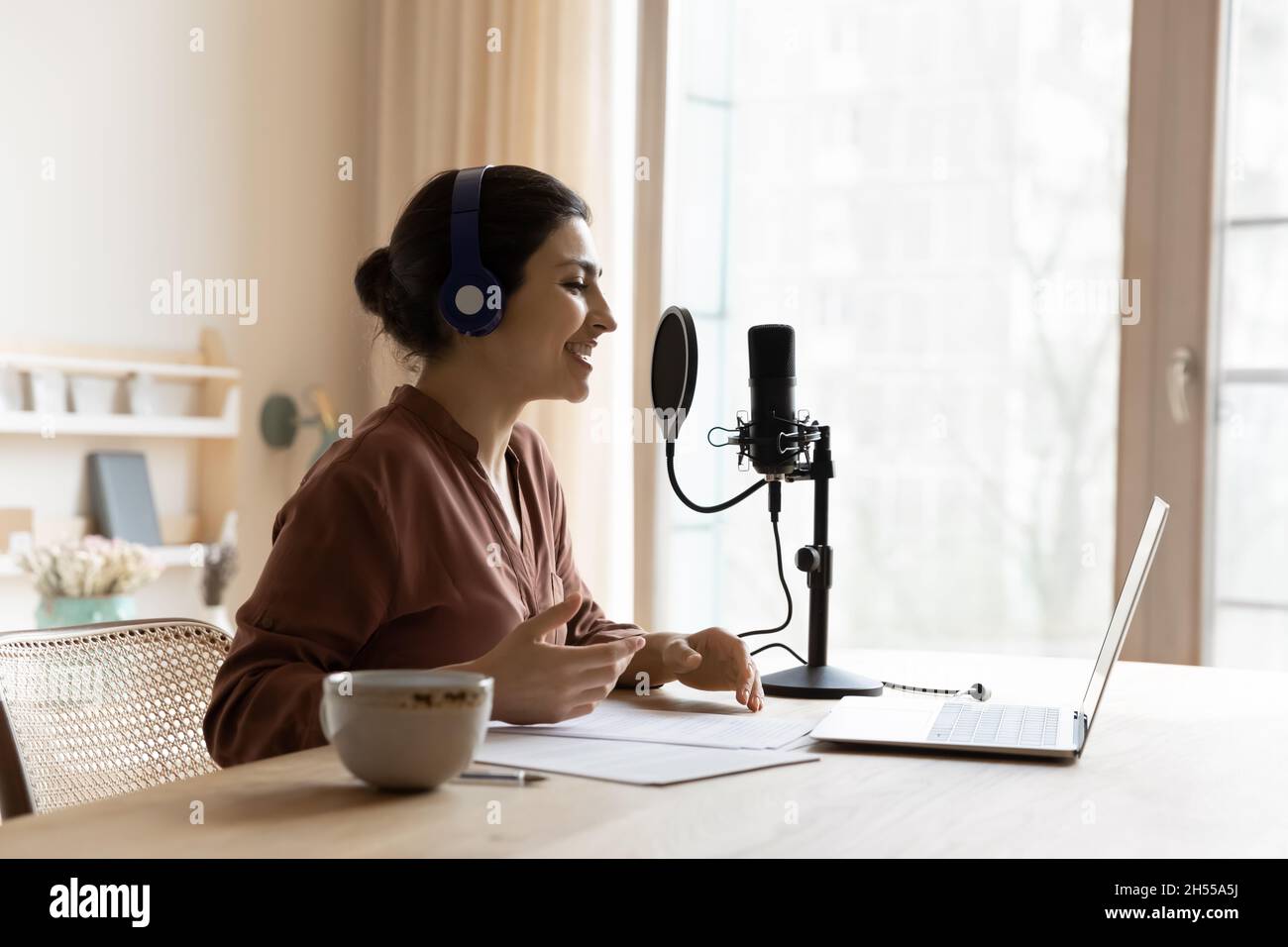 Woman wear headphones recording podcast on laptop talks using microscope Stock Photo