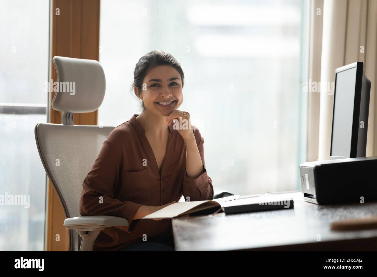 Smiling attractive Indian businesswoman sitting at desk pose for camera Stock Photo