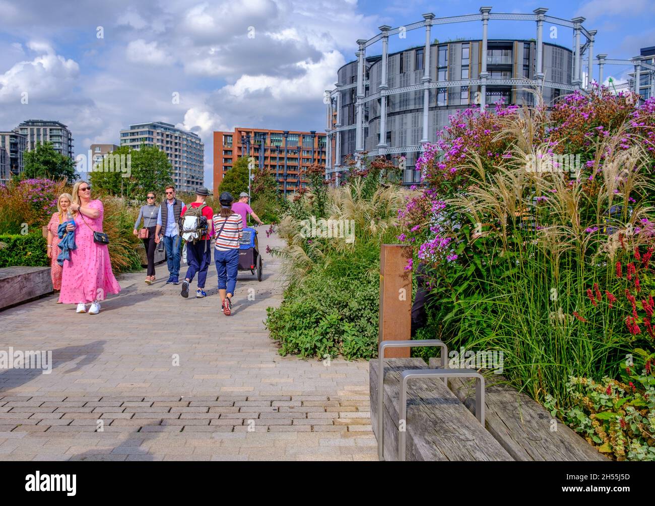 People walking on Bagley Walk an elevated park built on an old railway viaduct at King’s Cross, London with tall buildings in background. Stock Photo