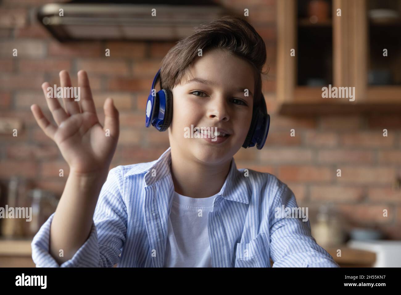 Junior school age boy in headphones wave hand to webcam Stock Photo