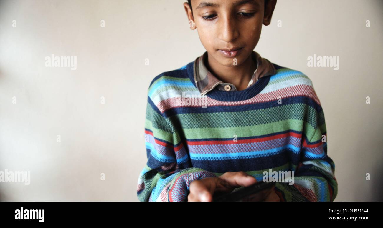 A closeup of a south Asian young boy with a colorful pullover playing with a phone Stock Photo