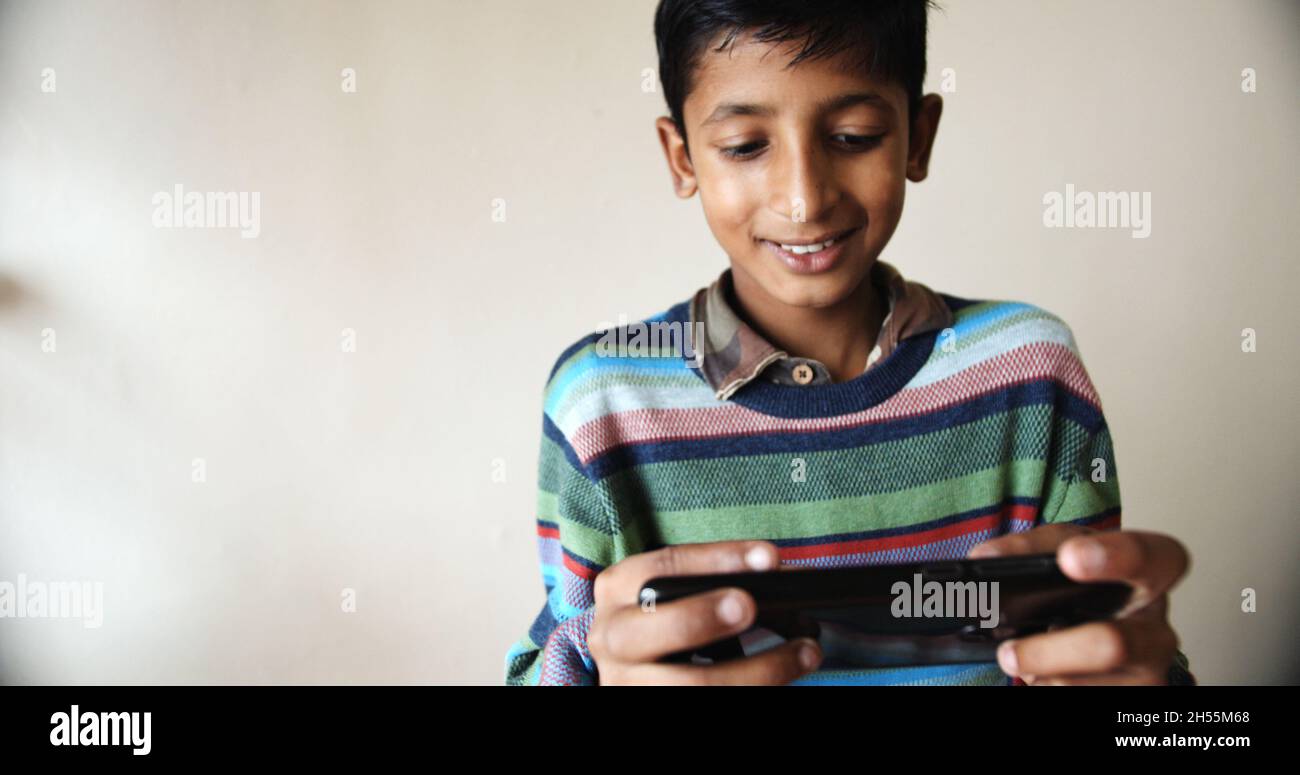 A Closeup of a south Asian young boy with a colorful striped pullover playing with a phone Stock Photo