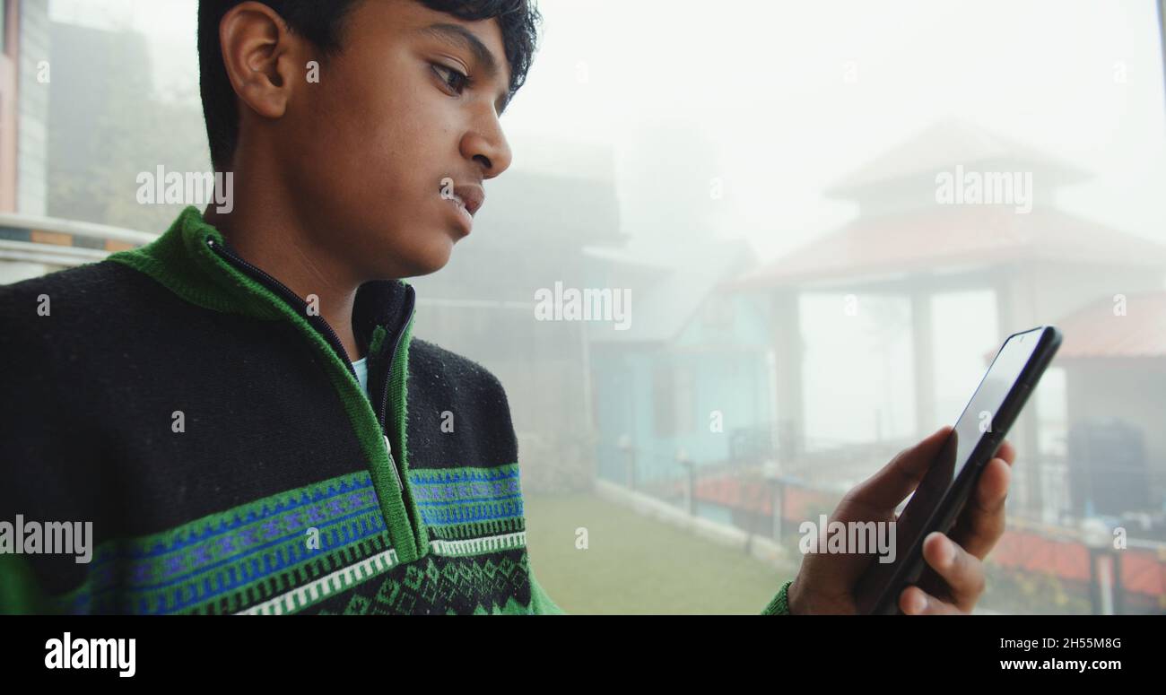 A Closeup of a south Asian young boy with a colorful striped pullover playing with a phone Stock Photo