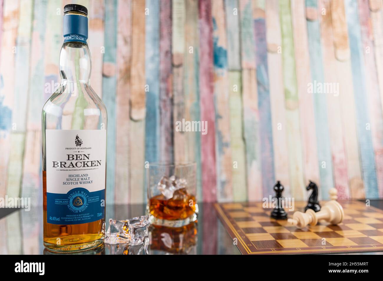 bottle of Ben Bracken Single malt whiskey with a glass, chessboard and ice cubes in front of a colorful wooden background Stock Photo