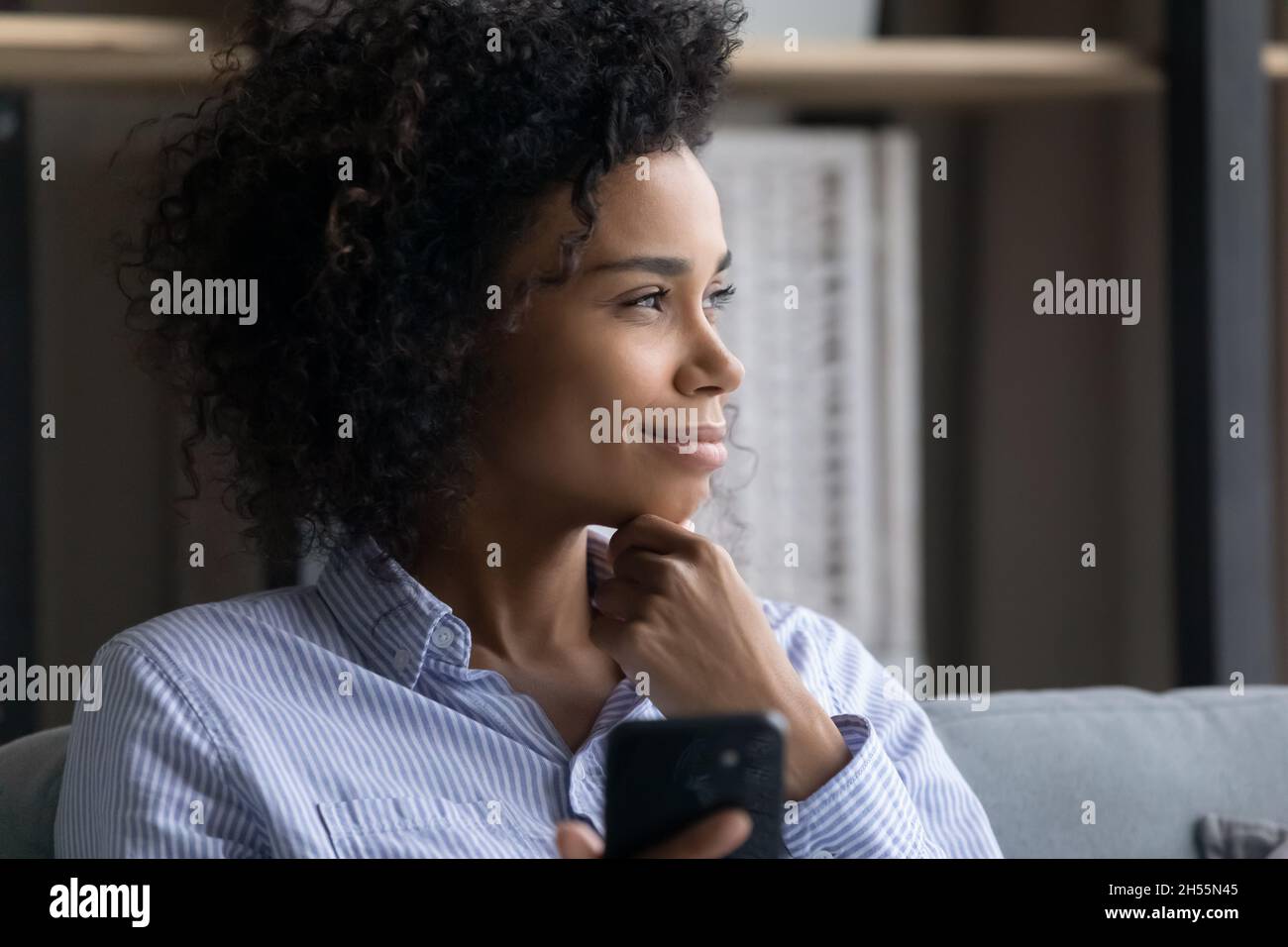 Close up profile smiling dreamy African American woman holding smartphone Stock Photo