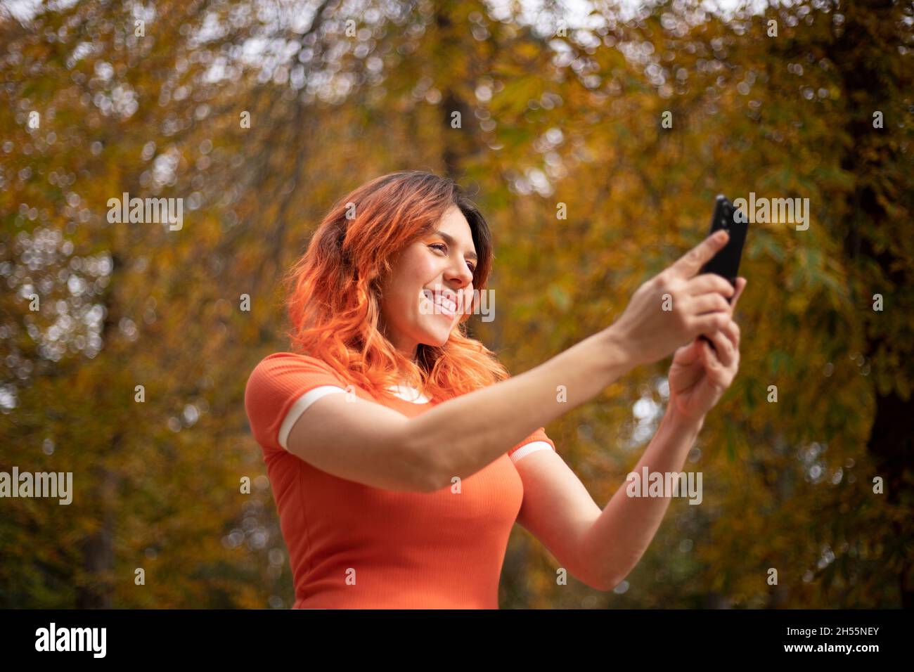 happy red-haired woman with cell phone in hand in a park in autumn Stock Photo