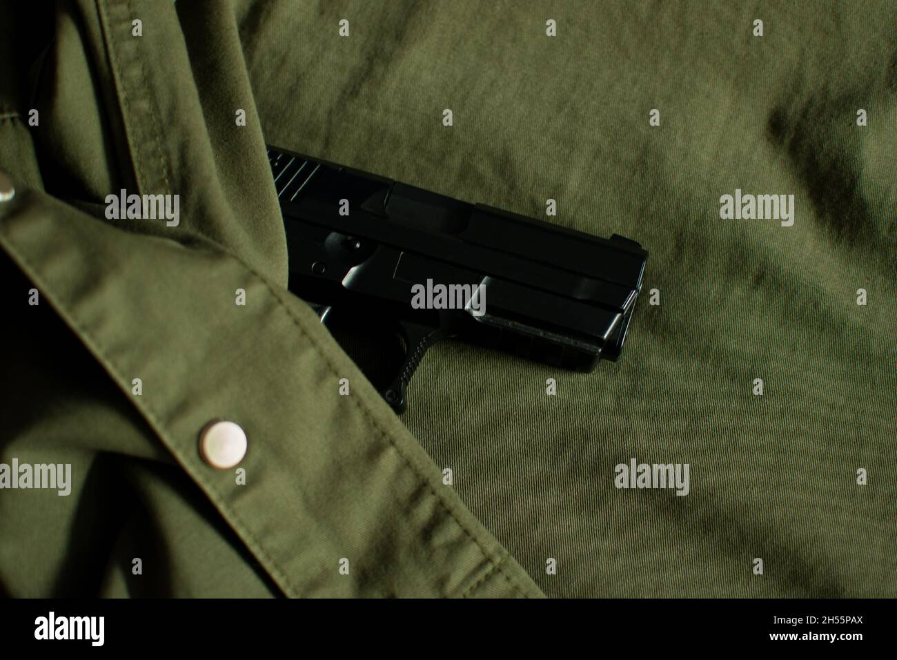 Black handgun, pistol hidden under vintage olive green military uniform Stock Photo