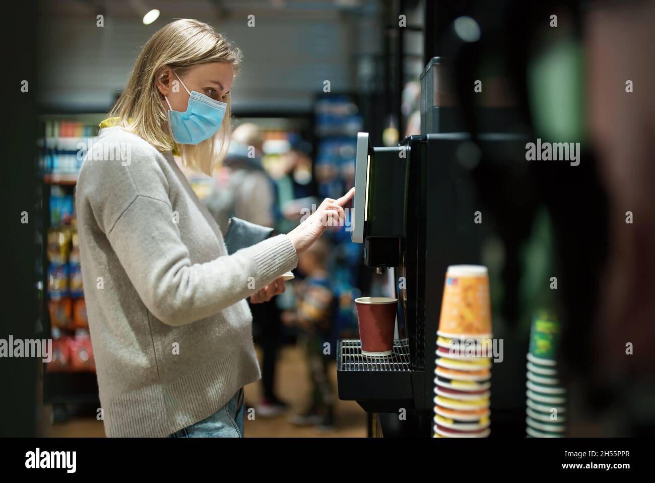 Woman in mask using coffee vending machine. Stock Photo