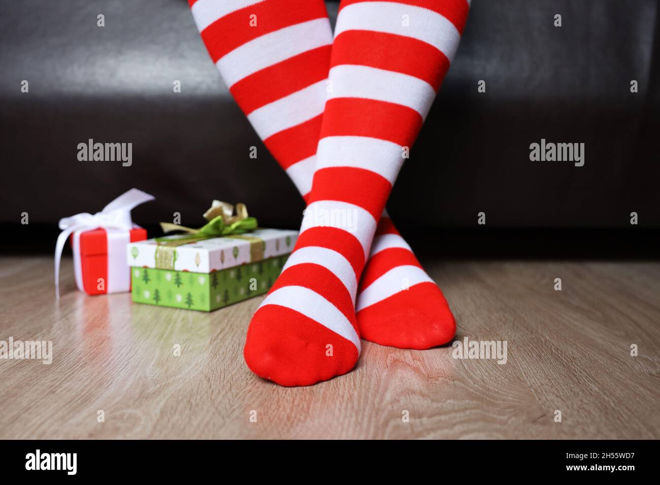 Female legs in Christmas knee socks on a floor near the gift boxes. Woman sitting on a bed in home, New Year celebration Stock Photo
