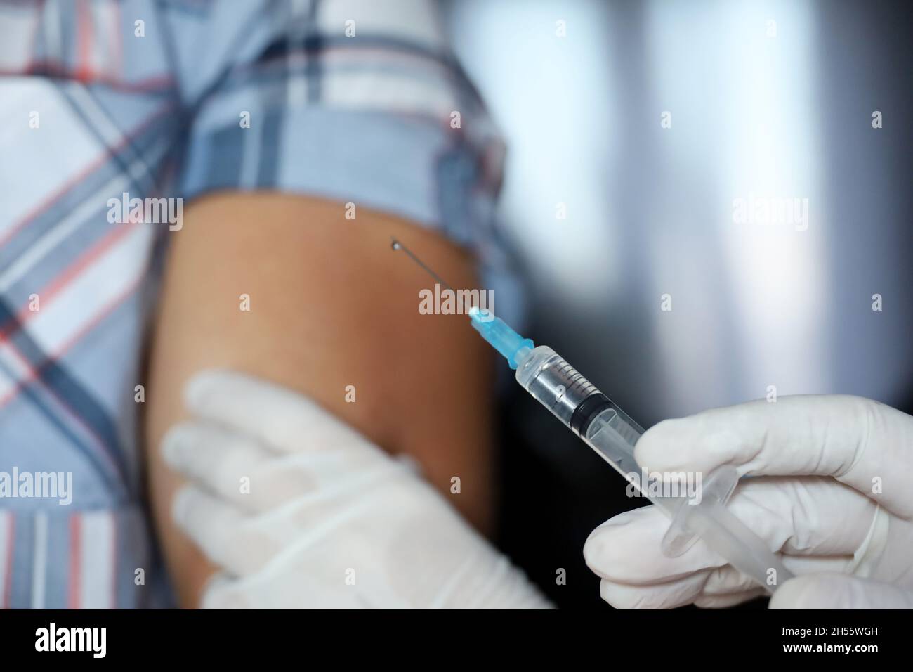Vaccination during covid-19 pandemic, female hand in protective glove with syringe. Nurse preparing to injection into a male shoulder Stock Photo